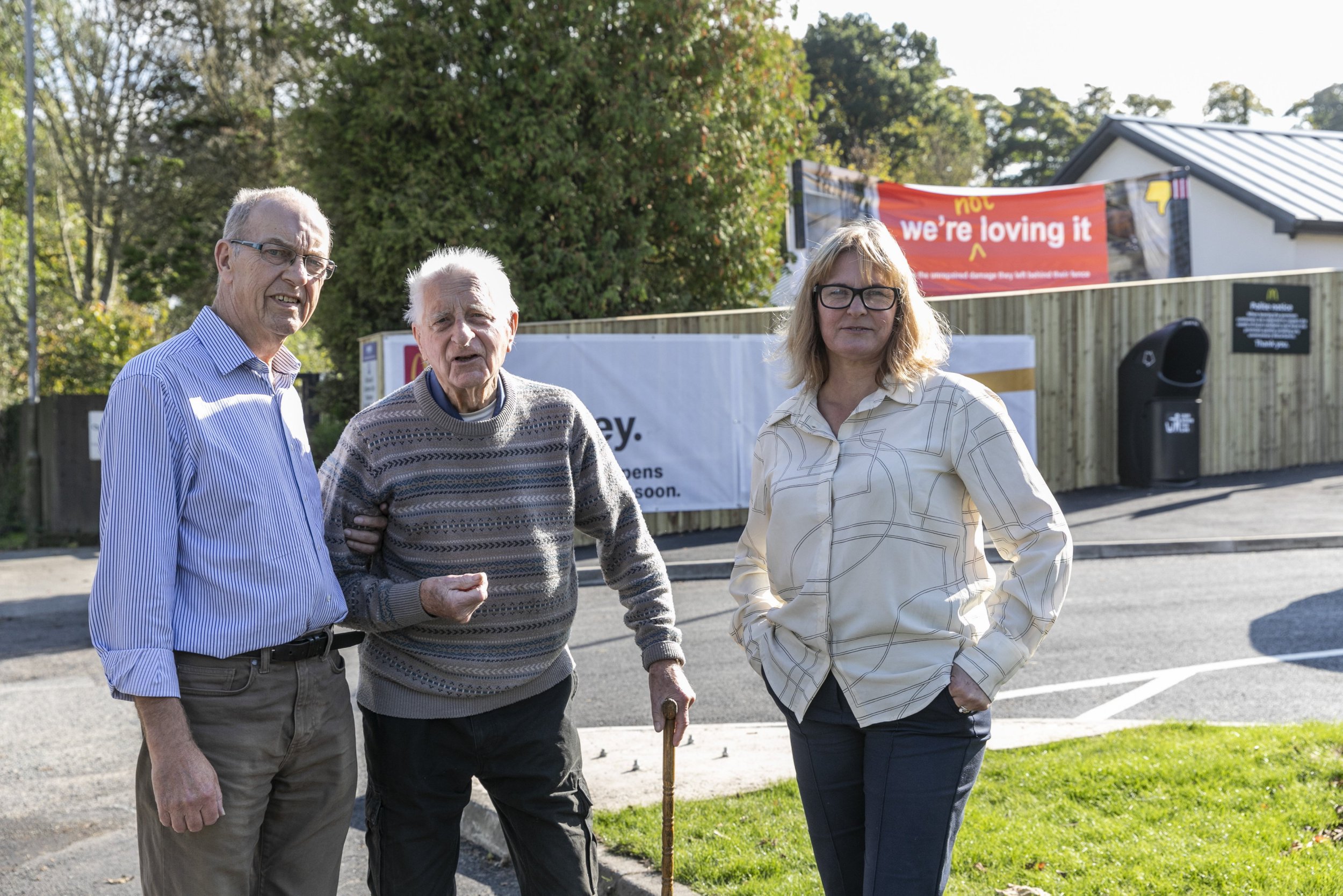 A woman with her husband and 91-year-old dad and a sign she has erected near a McDonald's restaurant car park.